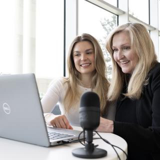Two women look at a computer screen together with a microphone next them