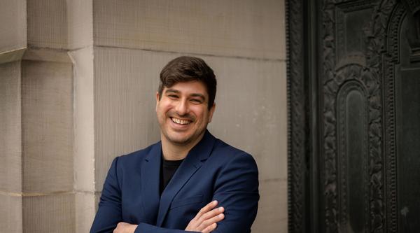 Michael MacKenzie standing against a wall and smiling at the camera.