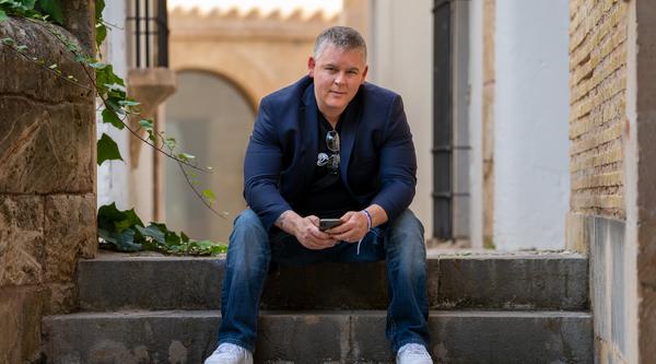 Morgan Carey sits on grey steps with an urban landscape behind him