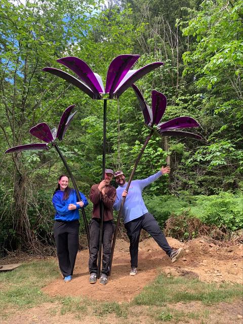 Three people stand under three giant flowers
