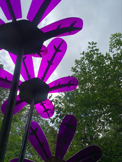 Three purple metal flowers with the sky in the background